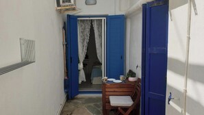 Een smalle gang met een blauwe deur die naar een kamer leidt. In de kamer staat een klein tafeltje met een stoel en een potplant.
