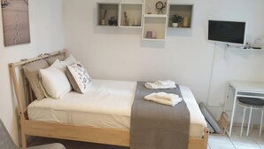 Een slaapkamer met een houten bed, witte beddengoed, een grijze plaids en een bureau met een stoel.