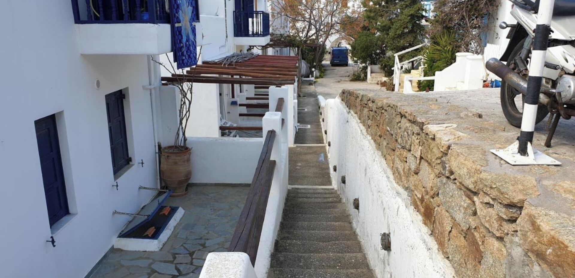 A narrow stone staircase leading up to a white building with a wooden bench and a potted plant.