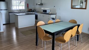 A modern kitchen with white cabinets, a central island, and a dining area with a glass table and wooden chairs. - Views, space and tranquility with bay and beach close by (Encounter Bay)