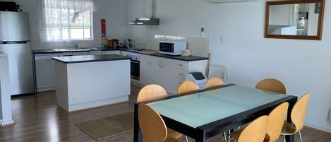 A modern kitchen with white cabinets, a central island, and a dining area with a glass table and wooden chairs.