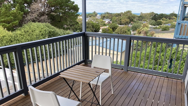 A wooden deck with a table and two chairs, overlooking a residential area with trees and houses. - Views, space and tranquility with bay and beach close by (Encounter Bay)
