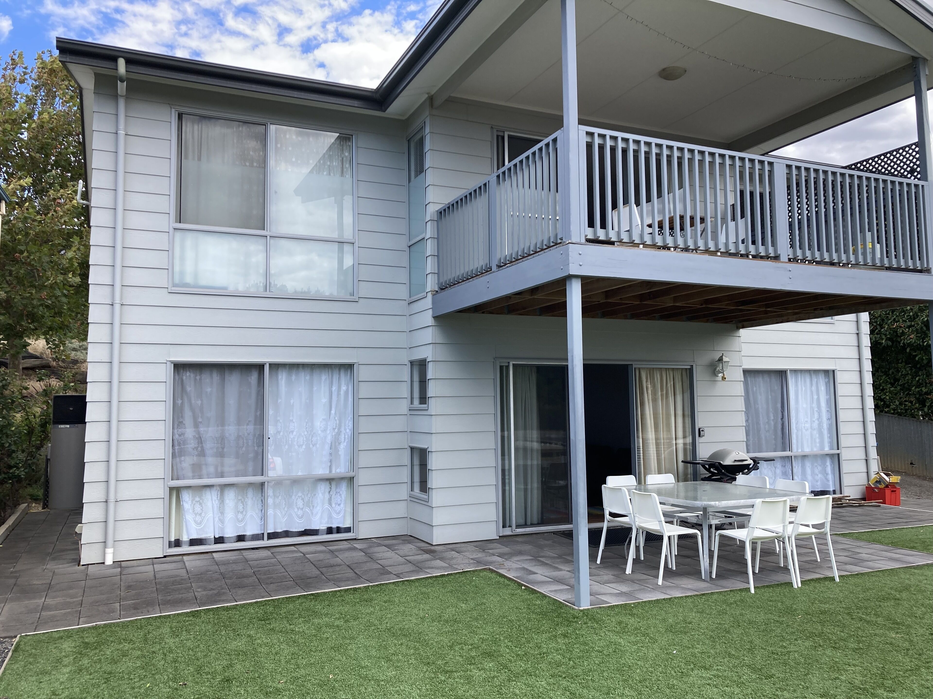 A two-story building with a balcony, a patio with a table and chairs, and a grassy lawn.