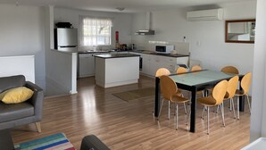 A modern kitchen with white cabinets, a central island, and a dining area with a glass table and wooden chairs. - Views, space and tranquility with bay and beach close by (Encounter Bay)