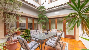 Un patio espacioso con una mesa de vidrio rodeada de sillas estampadas, plantas en macetas y un suelo de baldosas.