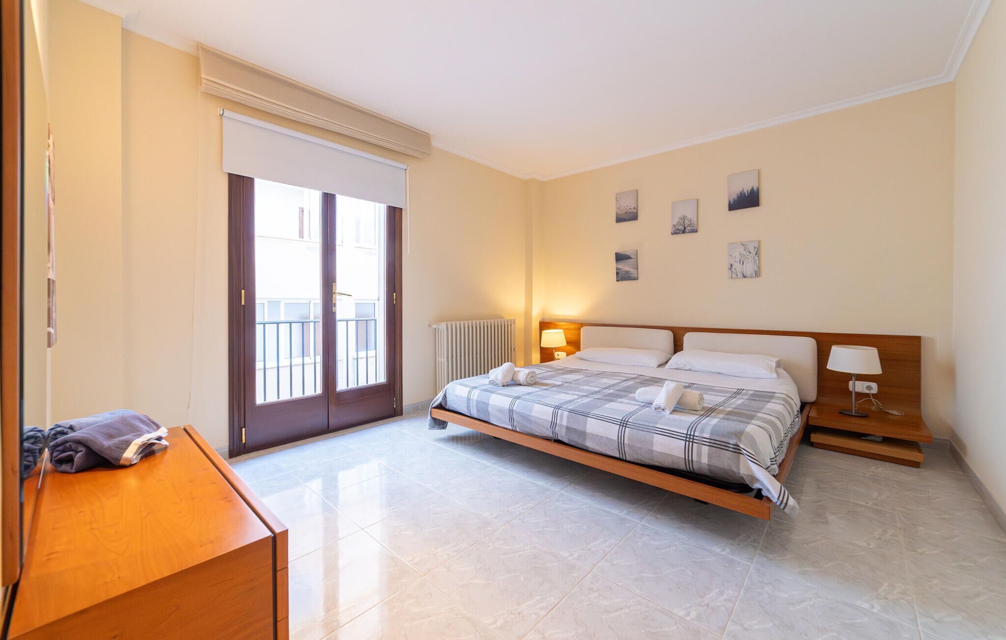 A bedroom with a bed, bedside tables, a radiator, a window with a view, and artwork on the wall.