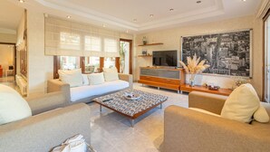 Un salón moderno con sofá, mesa de centro, televisor y un cuadro grande con un paisaje urbano.