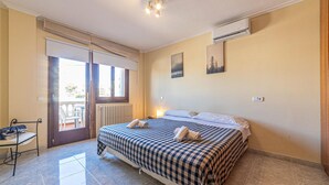 Una habitación de hotel con una colcha a cuadros, vistas a través de una puerta corredera, un radiador y un cuadro en la pared.