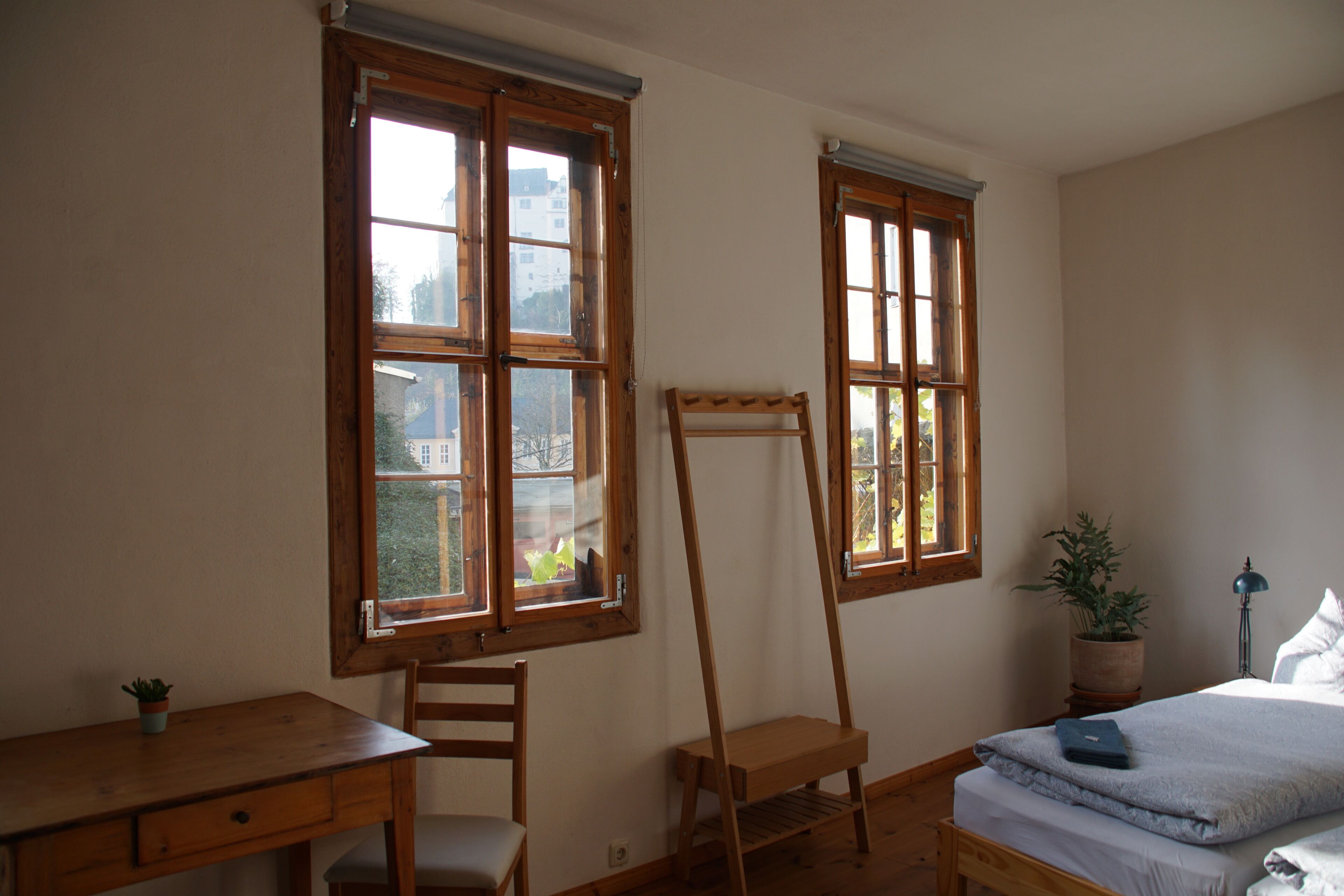 Ein Schlafzimmer mit einem Holztisch, einem Stuhl, einem Bett und zwei Fenstern.