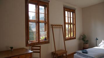 Ein Schlafzimmer mit einem Holztisch, einem Stuhl, einem Bett und zwei Fenstern.