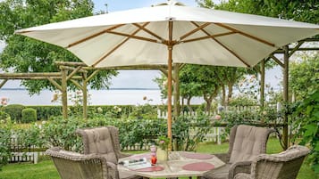 Ein Pavillon mit großem Sonnenschirm, Korbstühlen, einem runden Tisch und Meerblick.