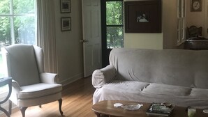 Un soggiorno con un divano grigio, una poltrona bianca, un tavolino in legno e una porta che dà su un balcone.