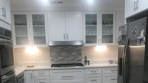 Una cucina moderna con mobili bianchi, un frigorifero in acciaio inossidabile, un piano cottura a gas e un pavimento decorato.