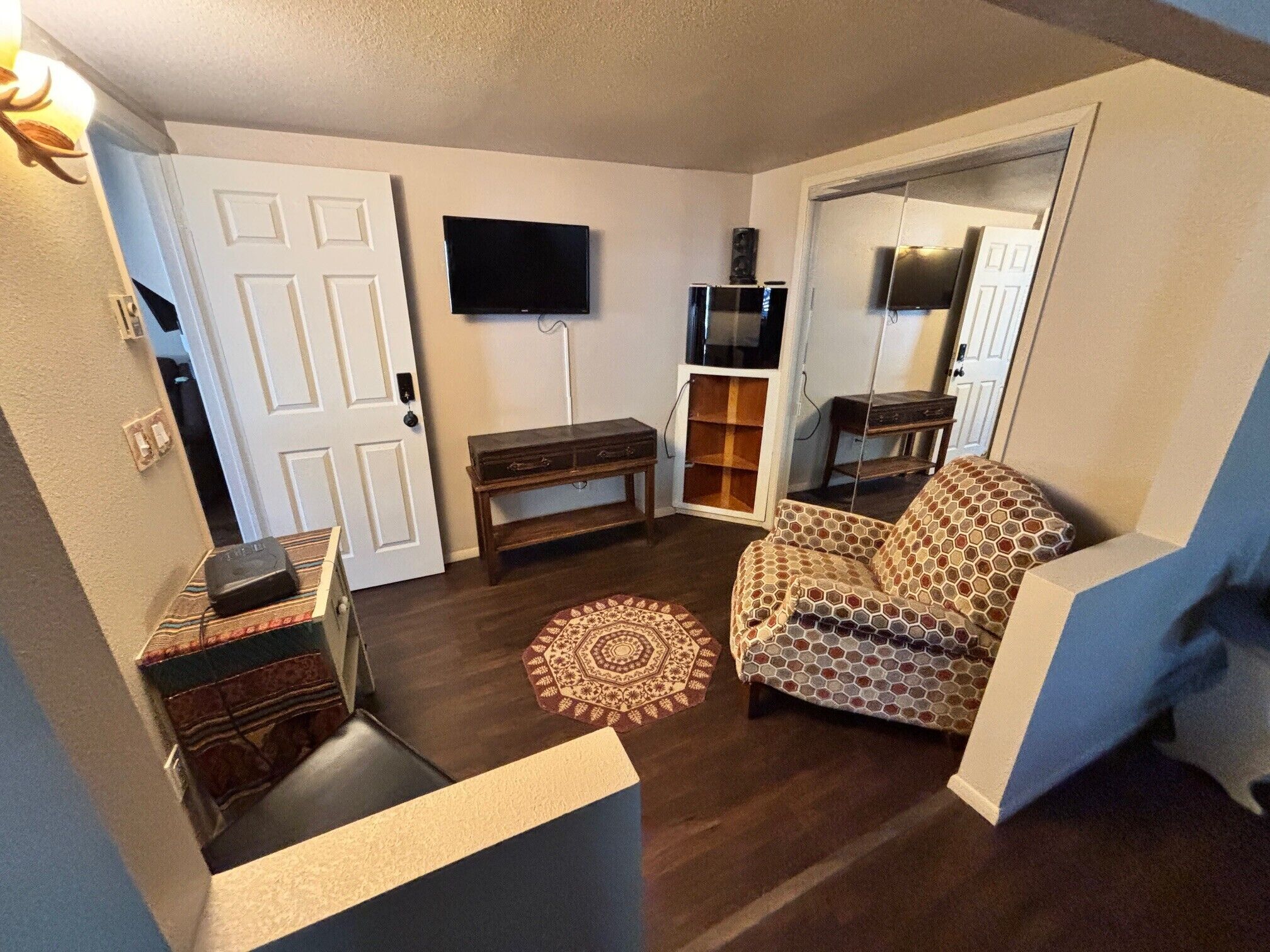 A living room with a television, a patterned armchair, a wooden bench, and a decorative rug.