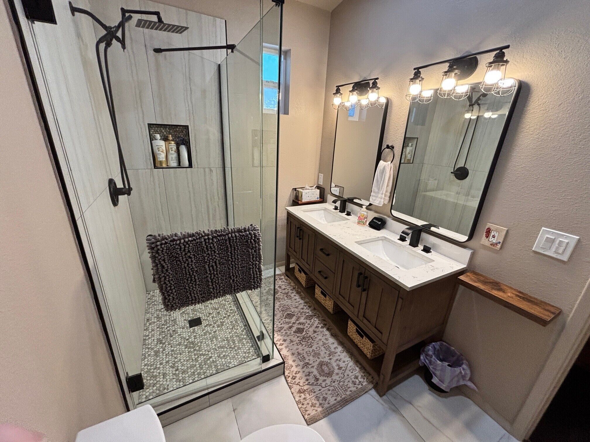 A modern bathroom with a glass-enclosed shower, a vanity with a double sink, and a large mirror with lights.