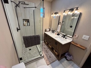A modern bathroom with a glass-enclosed shower, a vanity with a double sink, and a large mirror with lights.