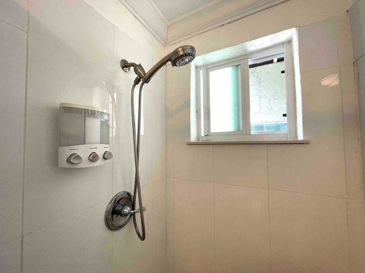 A bathroom with a shower, a window, and a control panel.