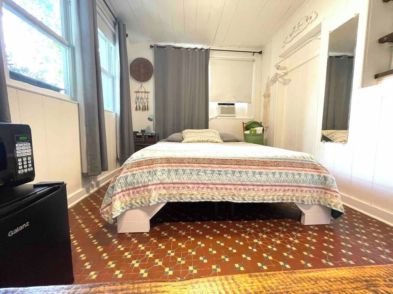 Habitació d'hotel amb un llit, escriptori amb telèfon, radiador i finestra amb cortines.