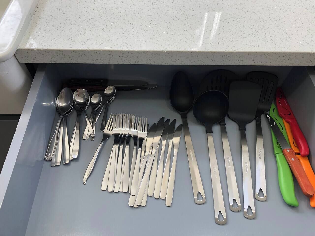 En skuffe med diverse bestik, herunder skeer, gafler, knive og et par tang.