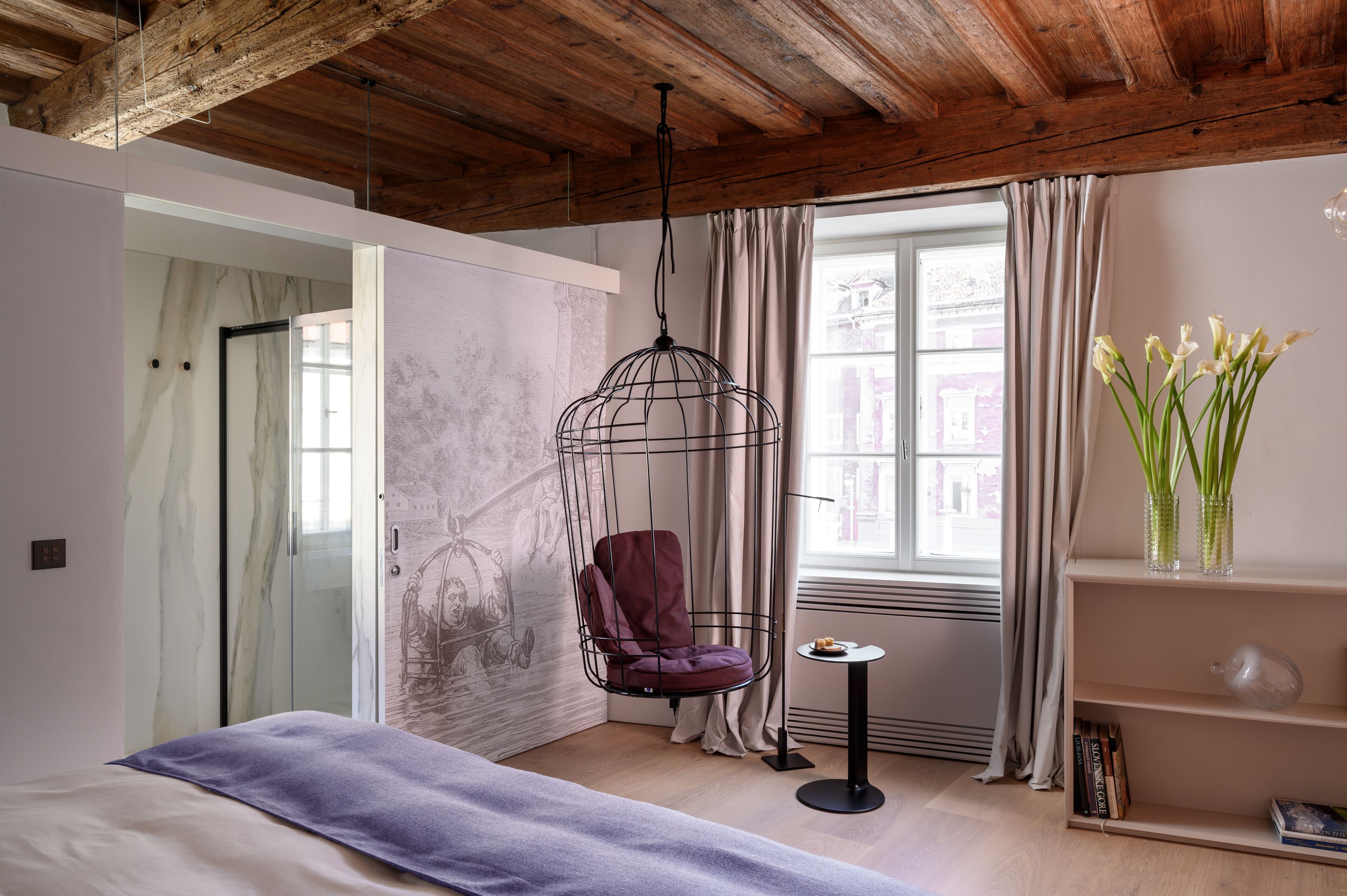 Quarto com cadeira suspensa, cama, mesinha com um vaso de flores e estante.