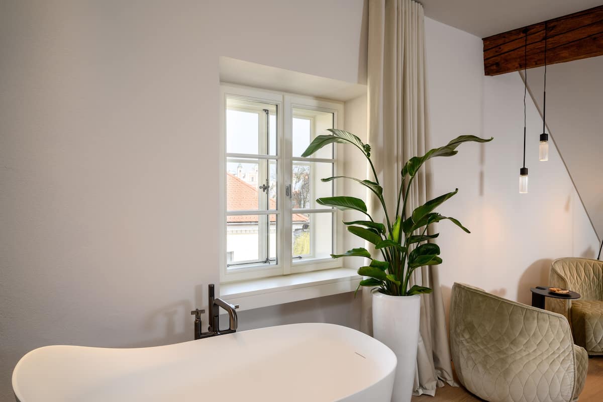 Ein modernes Badezimmer mit freistehender Badewanne, einem Topf mit Pflanze und einem blickdichten Fenster.