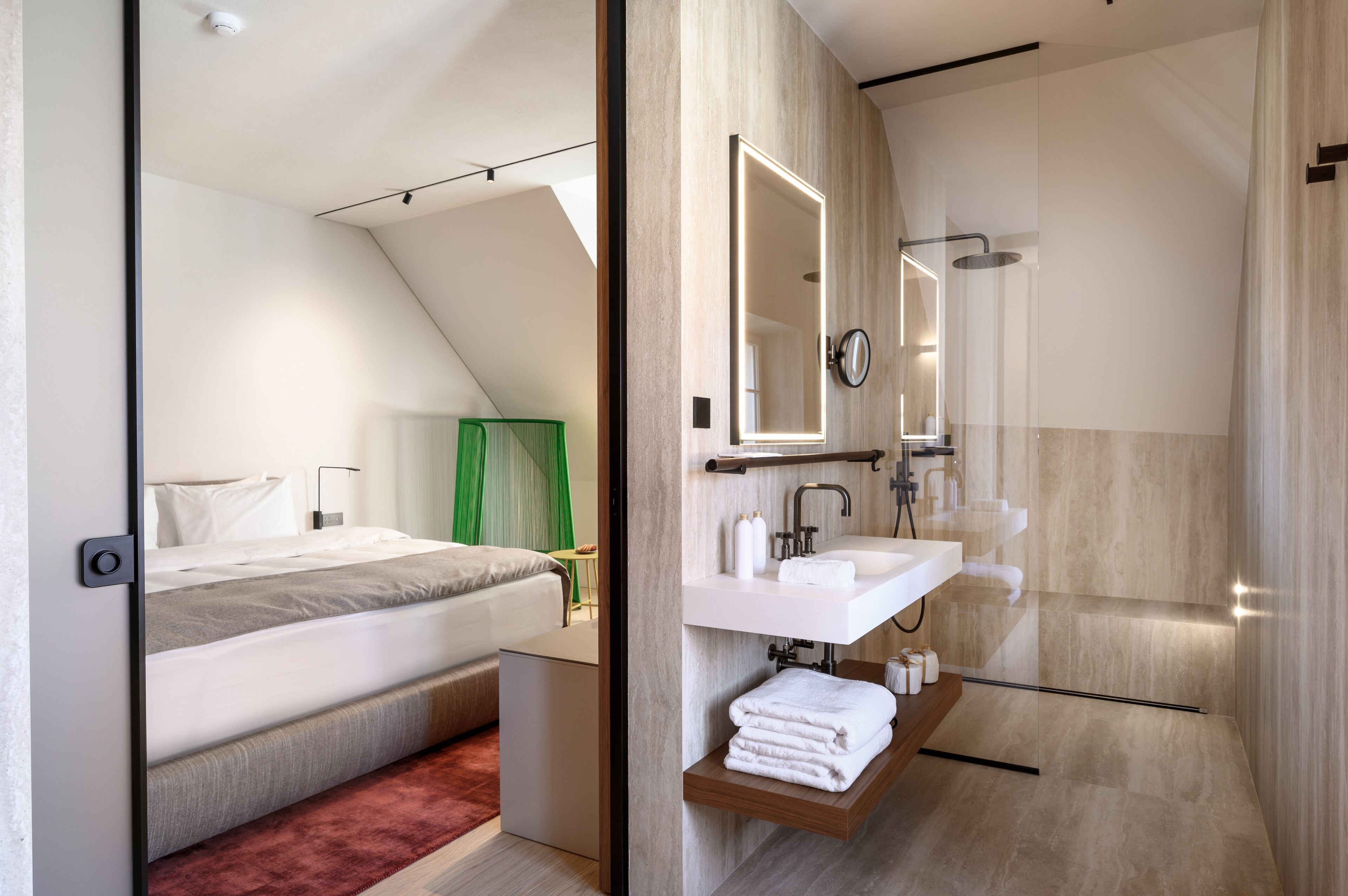 A modern bedroom with a bed, bedside table, and a green curtain. The image also shows a bathroom with a sink, mirror, and shower.