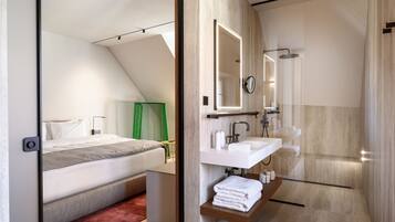 A modern bedroom with a bed, bedside table, and a green curtain. The image also shows a bathroom with a sink, mirror, and shower.