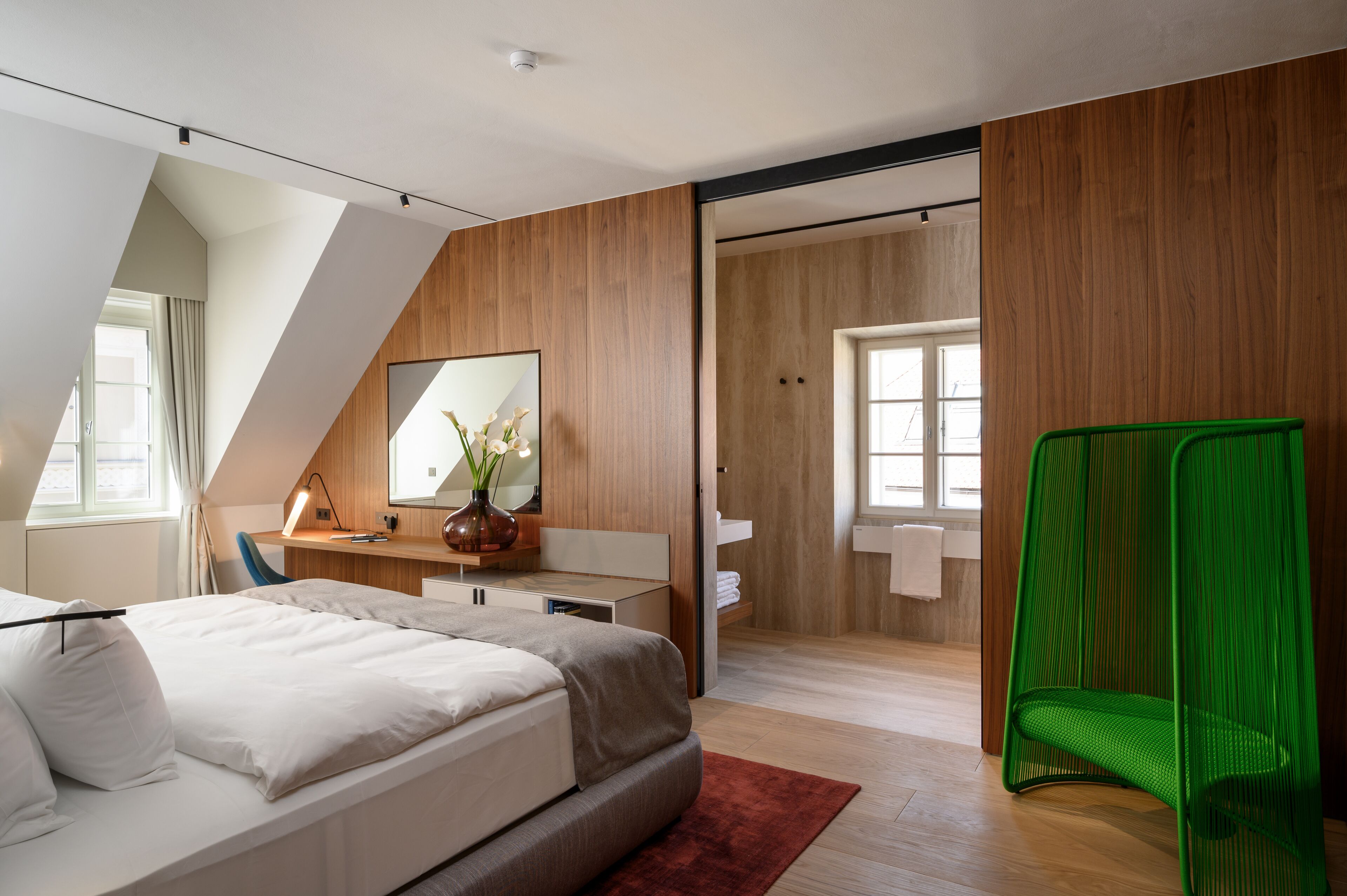 A modern bedroom with a bed, a desk, a mirror, and a green chair.