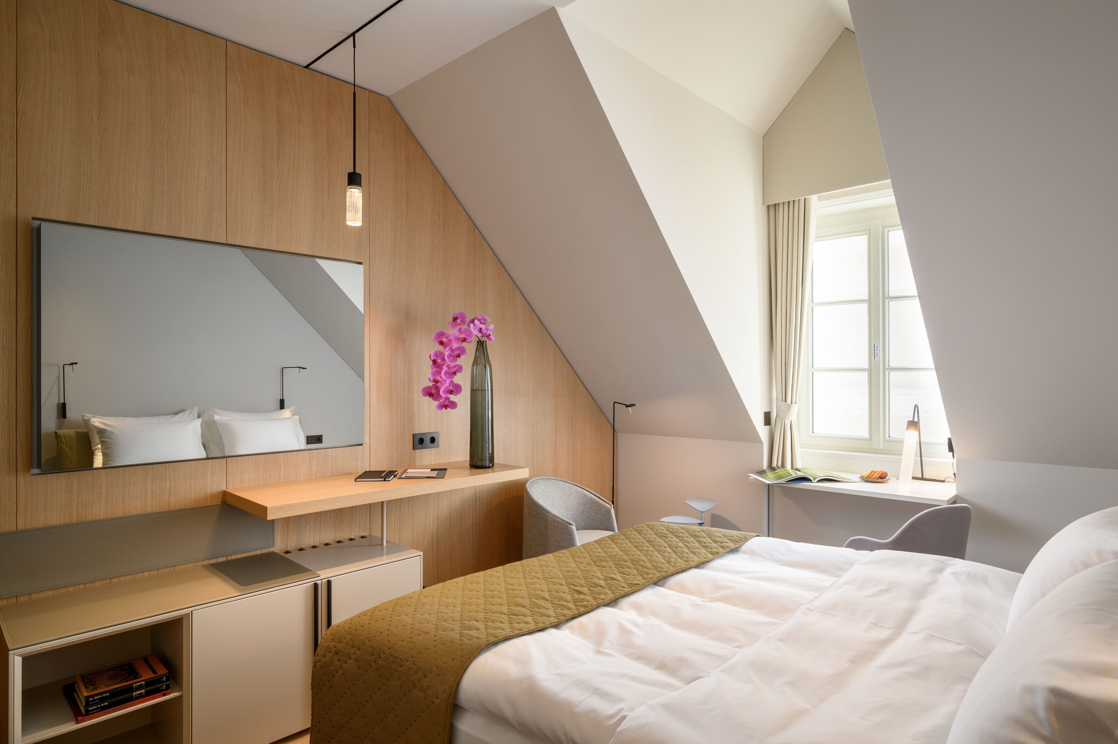 Habitación de hotel moderna con una cama grande, un escritorio, una silla, un espejo y una ventana con cortinas.