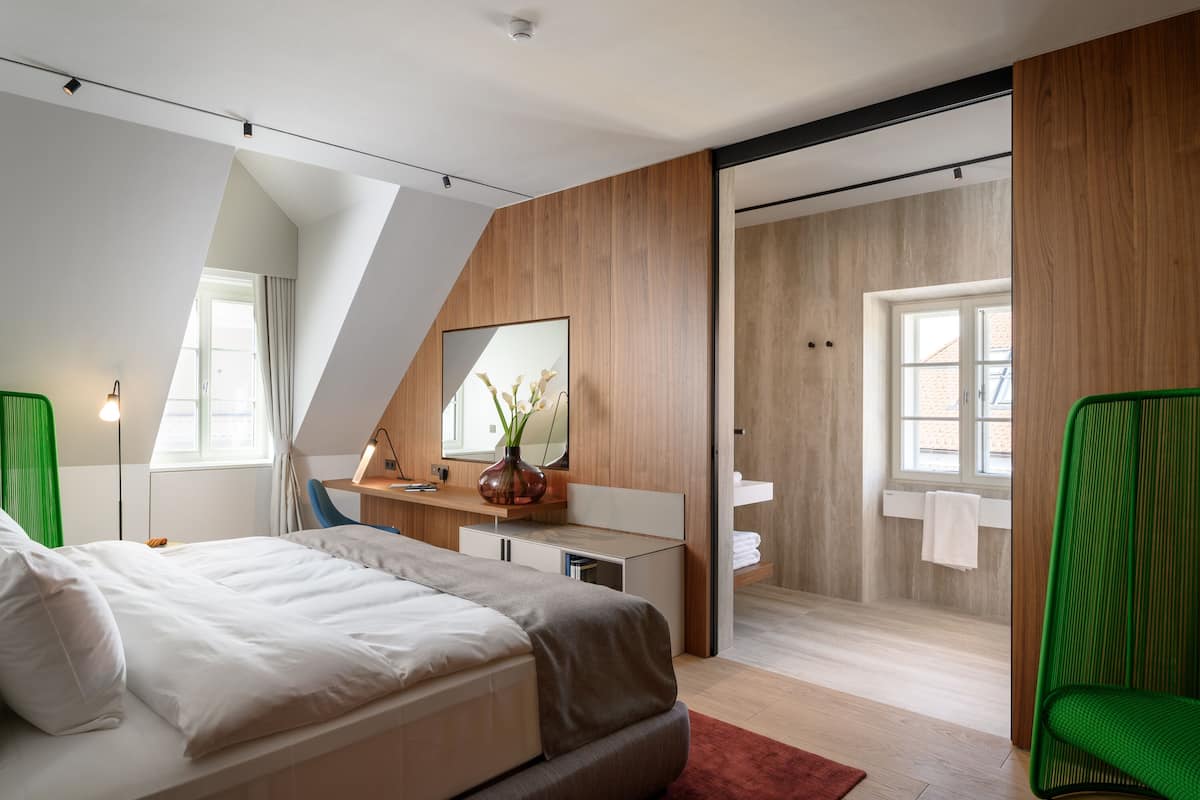 Ein modernes Schlafzimmer mit Bett, Schreibtisch, Spiegel und einem Badezimmer mit Dusche und Waschbecken.
