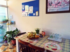 Un coin repas avec une table dressée pour deux personnes, un tableau d’affichage où sont accrochées diverses annonces et une plante en pot.