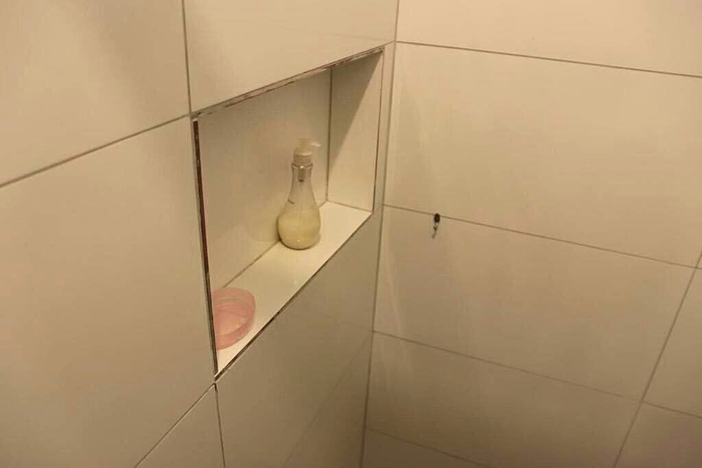 Ett badrum med vita kakelplattor, en hylla med en flaska och en tvålpump.