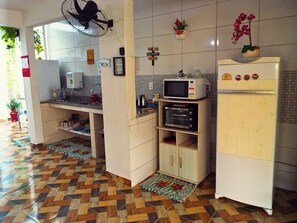Une cuisine équipée d’un four à micro-ondes, d’un four et d’un réfrigérateur. On y trouve également un ventilateur, une plante en pot et un pare-feu en carreaux.