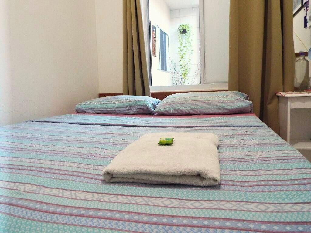 A bed with patterned bedding, a folded towel, and a window with curtains.