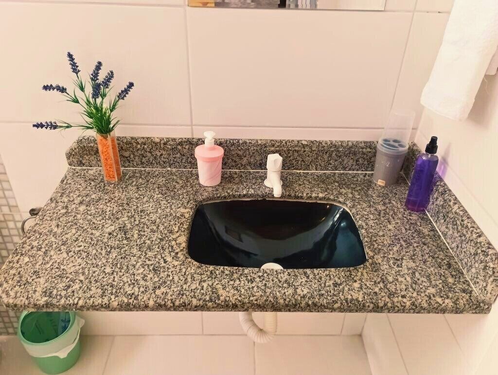 A kitchen with a granite countertop, a black sink, a small potted plant, a pink soap dispenser, and a white faucet.