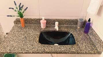 A kitchen with a granite countertop, a black sink, a small potted plant, a pink soap dispenser, and a white faucet.