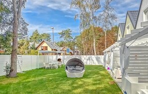 Relax in the serene backyard with a hanging chair amidst lush greenery and a charming house in the background.