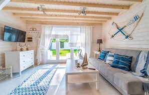 Relax in this spacious living room with a high ceiling, featuring a comfortable sofa, flat-screen TV, and a view of the lush garden.