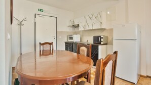 Een kleine keuken met een eettafel, stoelen, een magnetron, een broodrooster en een koelkast.