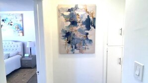 Ein Flur mit einem modernen, abstrakten Gemälde an der Wand, einer weißen Tür und einer Deckenleuchte.