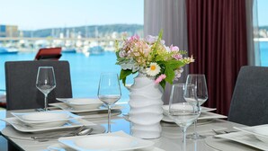 Une table à manger dressée avec des assiettes, des couverts et des verres à vin, et un vase de fleurs placé au centre.