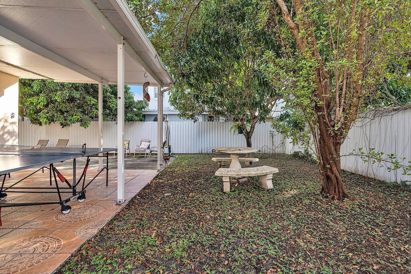 A covered patio area with a ping pong table, a stone bench, and a tree.