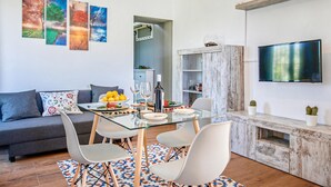 A modern living room with a glass dining table, white chairs, a grey sofa, and a TV mounted on the wall. - Nice home in Constantina (Constantina)