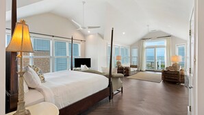 A spacious bedroom with a large bed, a ceiling fan, and a view of the ocean through large windows. - Ocean View Home in Gated Wild Dunes on Golf Course & Pool Access! (Isle of Palms)