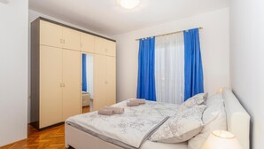 A bedroom with a bed, a wardrobe, and a window with blue curtains. - Cozy apartment in Malinska with WiFi (Malinska)