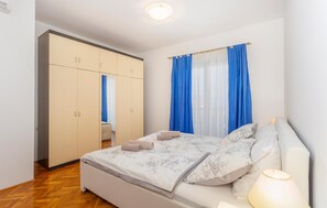 A bedroom with a bed, a wardrobe, and a window with blue curtains. - Cozy apartment in Malinska with WiFi (Malinska)