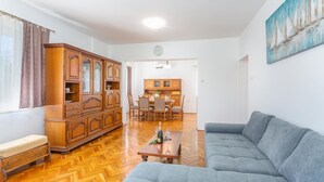 A spacious living room with a large grey sofa, wooden flooring, a dining area with a table and chairs, and a kitchen in the background. - Cozy apartment in Malinska with WiFi (Malinska)