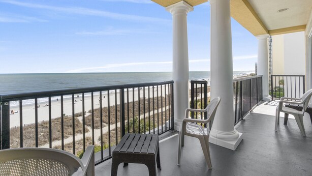 Un balcon avec des colonnes blanches, une vue sur la plage et une chaise.