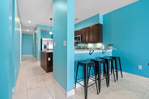 A modern kitchen with teal walls, a central island, bar stools, and a microwave.
