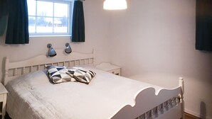 A bedroom with a white bed, a nightstand, a window with curtains, and wall-mounted lamps. - Stunning home in Grimslöv with sauna (Grimslöv)